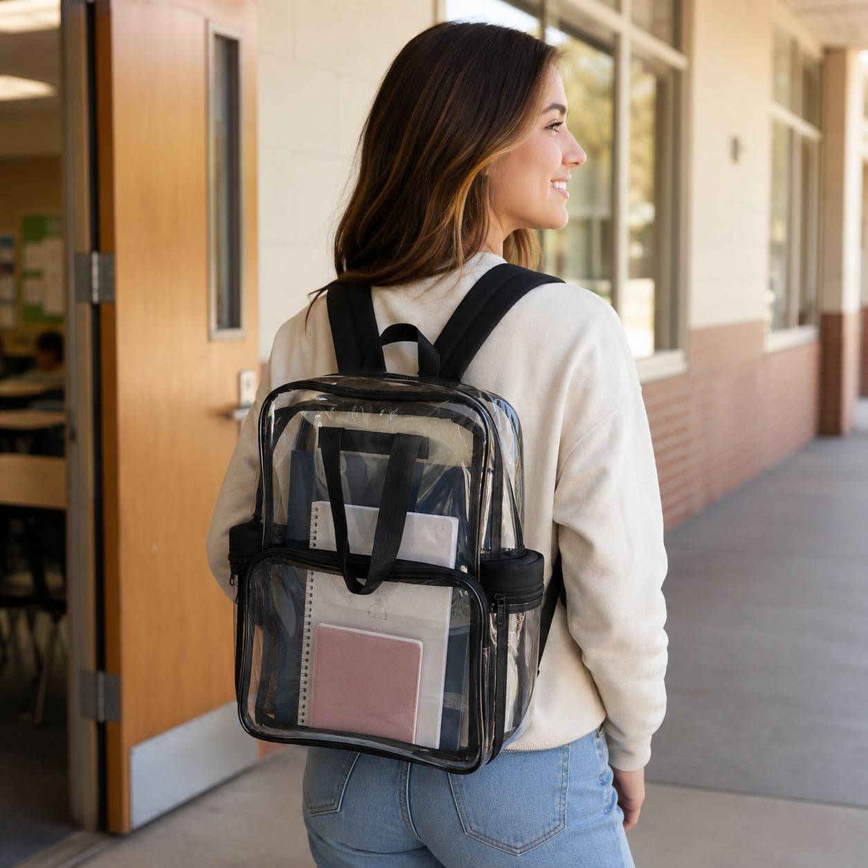 Woman wearing the clear backpack with cloth bottom, packed with notebooks, while walking into a school building.