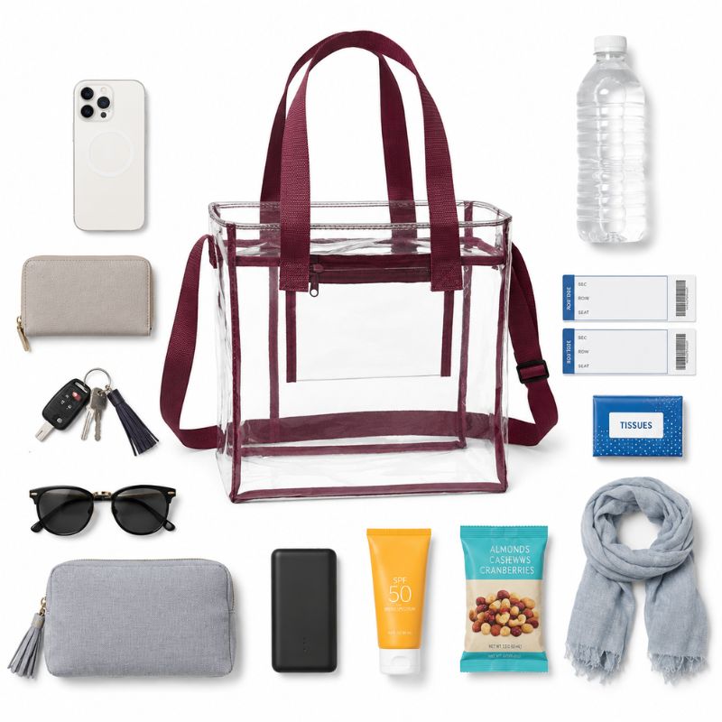 Burgundy-trim clear tote surrounded by everyday event essentials including a phone, wallet, keys, sunglasses, water bottle, tissues, charger, and small pouch.