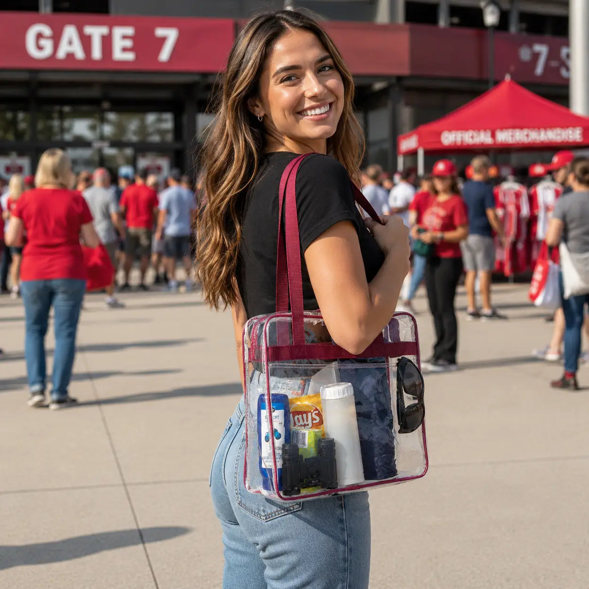 Woman carrying a clear stadium tote bag with burgundy trim at a stadium entrance