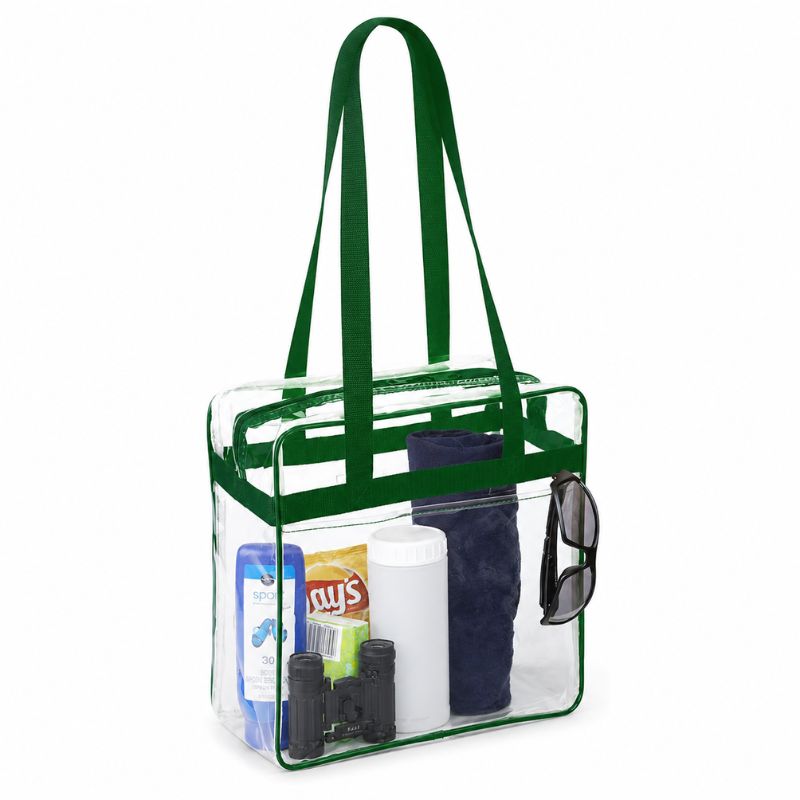 Clear stadium tote with green trim packed with sunscreen, chips, a rolled towel, and sunglasses.