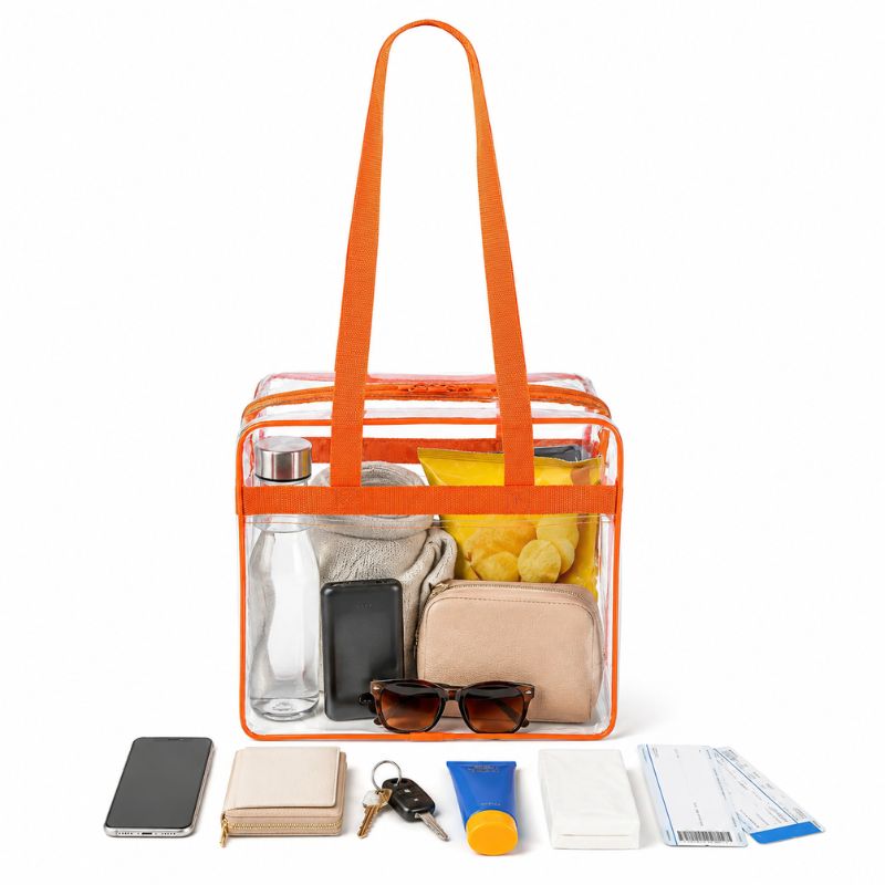 Clear stadium tote with orange trim packed with a water bottle, chips, sunglasses, and a coin pouch.