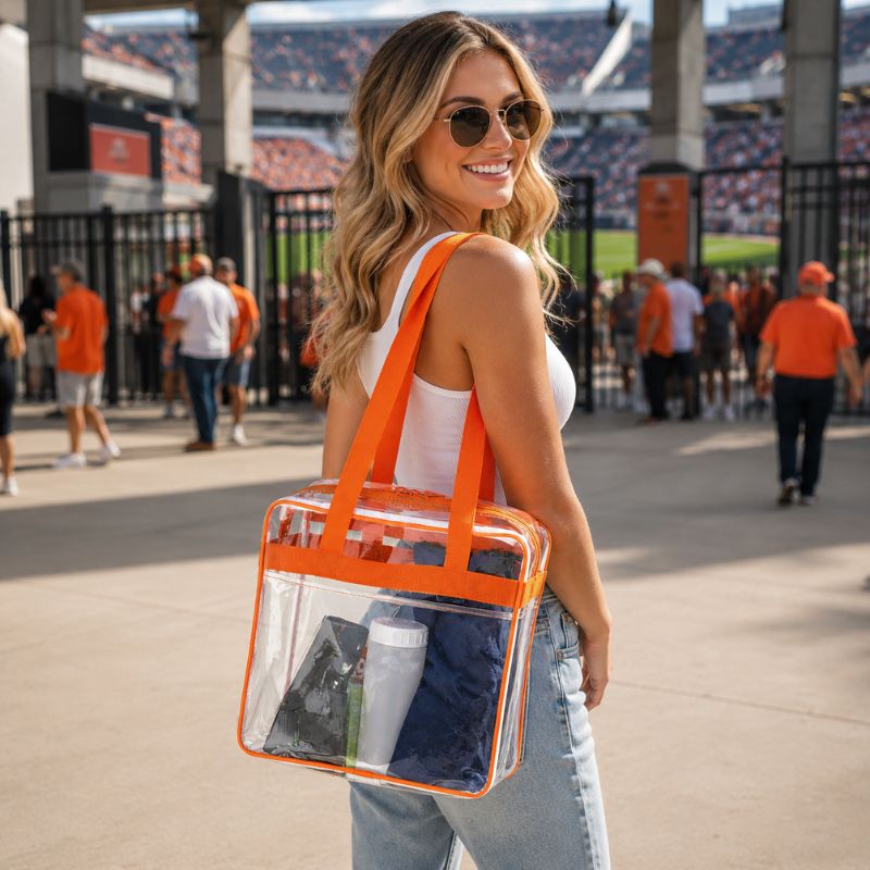 Woman carrying the clear stadium tote with orange trim over her shoulder at a stadium entrance.