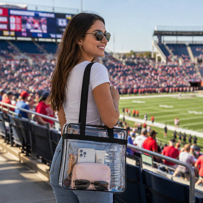 Woman carrying the clear stadium tote bag with black trim over her shoulder at a football stadium.