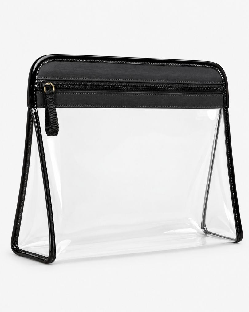 Clear makeup bag with black trim standing upright, showing the black top band, molded zipper teeth and gold-tone ring pull